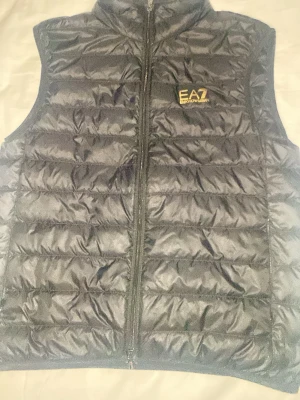  EA7 Emporio Armani väst - Snygg svart dunväst från EA7 Emporio Armani med gul logotyp på bröstet. Västen har quiltad design. Köpt på NK Göteborg.