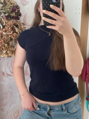 Mörkblå ärmlös topp med knappar - Stilren mörkblå ärmlös topp med rund hals och guldfärgade knappar på ena axeln. Mjuk och stretchig kvalitet, perfekt till jeans eller kjol. Enkel att matcha och ger en clean look.