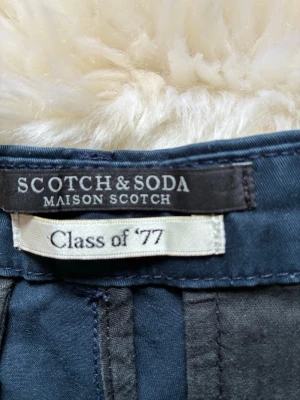 Mörkblå Slim Chinos Scotch & Soda - Snygga mörkblå slim chinos från Scotch & Soda, modell Class of '77. Byxorna har en smal passform och är tillverkade i ett mjukt bomullsmaterial. Perfekta för dig som gillar stilrena och bekväma byxor med modern look.
