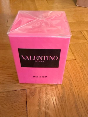 Valentino Donna Born In Roma parfym - Valentino Donna Born In Roma parfym i en snygg, fyrkantig rosa kartong med svart etikett och tydlig logga. Förpackningen är plastad och har en modern, lyxig känsla. Perfekt för dig som gillar exklusiva dofter och trendiga märken.