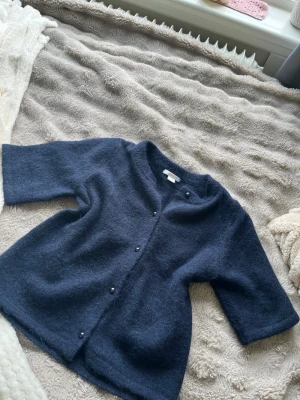Mörkblå kofta från Gina Tricot - Mysig mörkblå kofta från Gina Tricot med trekvartsärmar och knappar framtill. Koftan är fluffig och har en enkel, rak passform som passar perfekt till lager på lager. Materialet känns mjukt och behagligt mot huden.