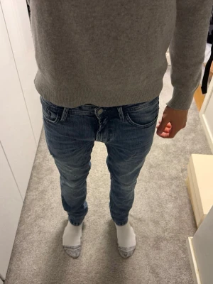 Blå slim fit jeans  - Säljer ett par blå slim fit jeans från Jack & Jones med lätt slitna detaljer och klassisk femficksdesign. Jeansen har normal midja och smal passform hela vägen ner. Perfekta för en avslappnad och trendig look.