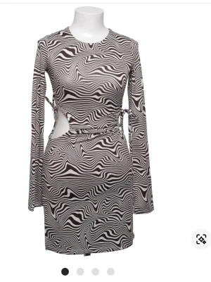 Zebramönstrad kort klänning med cut-outs - Snygg kort klänning med svartvitt zebramönster och långa ärmar. Klänningen har trendiga cut-outs i midjan och figurnära passform. Perfekt för dig som vill sticka ut med ett coolt mönster och unika detaljer. Anpassningsbar storlek då man kan göra cut outsen större eller mindre. 