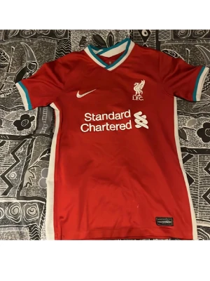 Liverpool matchtröja Nike röd - Liverpool FC matchtröja i rött med vita och turkosa detaljer. Tröjan har klubbmärke och Nike-logga på bröstet samt sponsortryck framtill. Tillverkad i lätt och ventilerande material, perfekt för fotbollsträning eller support.