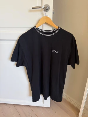 Svart t-shirt från Polar Skate Co - Svart t-shirt från Polar Skate Co med vit broderad logga på bröstet och ribbad krage med vita ränder. 