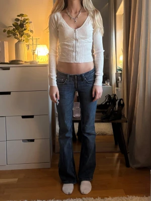 Snygg vit kofta med zip! - Snygga mörkblå jeans med bootcut-modell och låg midja. Jeansen har klassiska fickor fram och bak samt detaljerade sömmar. Perfekta för dig som gillar en tidlös och trendig denimlook.