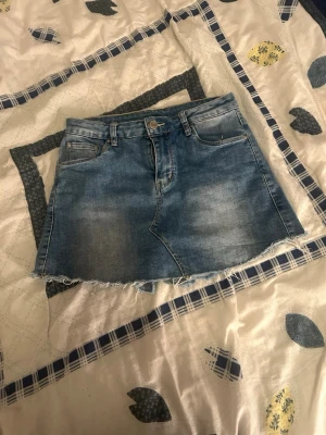 Blå jeansskort med rå kant - Säljer en snygg blå jeansskort med rå, fransig kant och klassisk femficksdesign. Skorten har bälteshällor, knapp- och dragkedjestängning samt två bakfickor. Perfekt för dig som gillar en avslappnad och trendig stil.