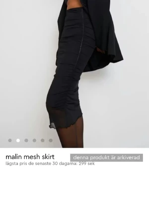 Svart mesh långkjol från Malin - Trendig svart långkjol i mesh med snygga rynkade detaljer längs sidorna. Kjolen har en figurnära passform och transparent nederkant som ger en cool och modern look. Perfekt att styla med en oversized skjorta eller crop top.