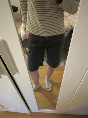 Mörkgråa jeansshorts i rak modell - Säljer ett par mörkgråa jeansshorts i rak och lite längre modell. Klassisk femficksdesign och stängs med dragkedja och knapp. Perfekta för en avslappnad och stilren look. Materialet är denim, vilket ger en cool och tidlös känsla.