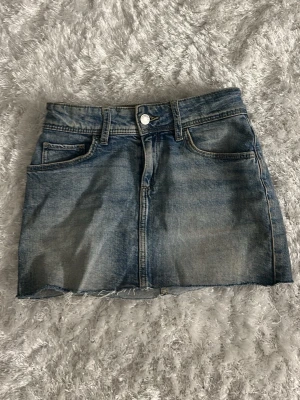 Jättefin blå jeanskjol - Snygg blå jeanskjol i klassisk modell med fem fickor och rå, avklippt kant nertill. Kjolen har bälteshällor och knappstängning framtill. Perfekt för dig som gillar en avslappnad och trendig stil. Vet ej vars den är ifrån, köpte från vinted men säljer då den var för liten på mig.