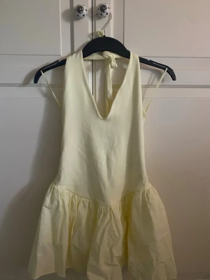 Ljusgul kort klänning med knyt - Söt ljusgul kort klänning med volangkjol och knyt i nacken. Klänningen är från Zara och säljs inte längre. Den är använd 1 gång och har inga märken!