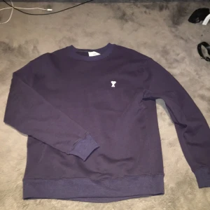 Vintage blå/lila - En stilren mörklila sweatshirt med rund hals och en liten vit broderad detalj på bröstet. Tröjan har långa ärmar, ribbade muddar och en avslappnad passform. Perfekt för en casual och trendig look.