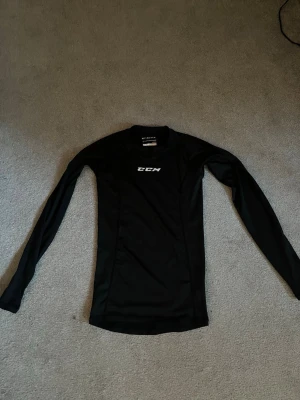 Svart långärmad träningströja CCM - Svart långärmad träningströja från CCM med vit logga på bröstet. Tillverkad i ett stretchigt och funktionsmaterial som passar perfekt för sport och träning. Tight passform och rund halsringning.