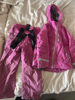 Rosa täckbyxor och jacka - Byxor och jacka i bra skick. Finns två små fläckar på ena benet. Storlek 130