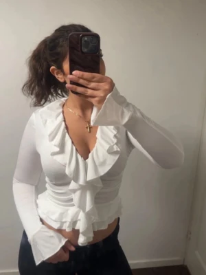 Vit volangblus med djup V-ringning - Gullig vit blus som passar bra till våren och sommaren. Endast använd en gång. 