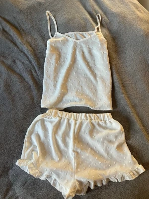 Vitt pyjamasset med volangdetaljer - Sött vitt pyjamasset med linne och shorts. Linnet har smala axelband och shorts med resår i midjan samt volangkant nedtill. Tunt, lätt material med diskret strukturmönster. Pyjamasen är från Gina tricot men etiketterna är borttagna💗str Xs men upplevs som större.💗