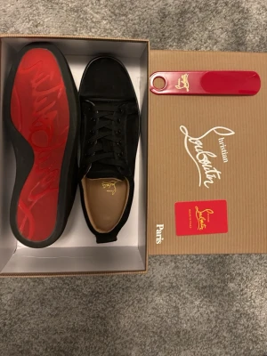 Christian Louboutin - Snygga svarta sneakers från Christian Louboutin med klassisk röd sula och diskret logga på innersulan. Skorna har ovandel i mocka, svarta skosnören och stilren design. Perfekta för dig som vill ha något exklusivt och trendigt.  Endast använda en gång !