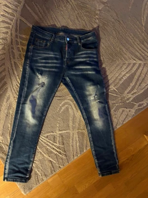 Mörkblå skinny jeans från Dsquared2 - Snygga mörkblå skinny jeans från Dsquared2 med slitningar och blekta detaljer på benen. Klassisk femficksmodell med knappgylf och Dsquared2-logga vid gylfen. Perfekta för en trendig streetstyle-look.