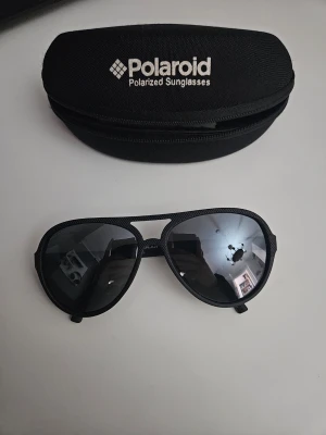 Svarta Polaroid pilot-solglasögon - Snygga svarta pilot-solglasögon från Polaroid med polariserade linser. Bågarna är i svart syntetmaterial och glasen har en mörk ton. Kommer med originalfodral. Perfekt accessoar för soliga dagar!