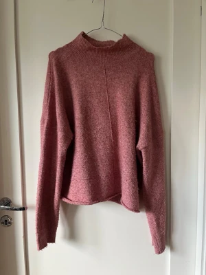 Rosa stickad tröja - Mysig rosa stickad tröja från NAKD med hög ribbad krage och lång ärm. Tröjan har en rak och något boxig passform med synlig söm framtill. Perfekt för lager-på-lager och chill dagar. Materialet känns mjukt och fluffigt.