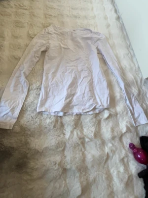 Vit långärmad topp från lager 157 - En basic vit långärmad topp från H&M med rund halsringning. Tillverkad i mjuk bomull som känns skön mot huden. Perfekt att styla lager på lager eller bära som den är. Enkel och clean design som passar till allt.