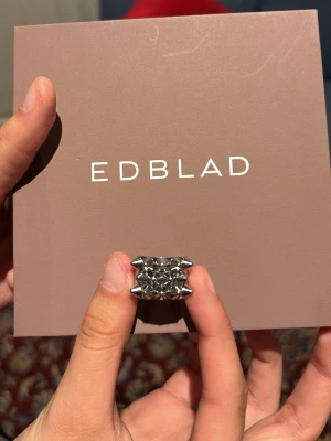 Silvrig ring med nitar från Edblad - Cool ring i silverfärgad metall från Edblad med ett unikt mönster av pyramidformade nitar runt hela ringen. Ringen har en chunky och edgy design som verkligen sticker ut och passar perfekt för dig som gillar statement-smycken.