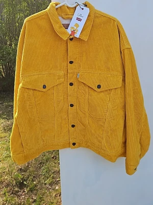 Gul manchesterjacka Levi's x Simpsons - Gul manchesterjacka från Levi's i samarbete med The Simpsons. Jackan har svarta knappar, två stora bröstfickor och en unik innerfodring med Simpsons-figurer. Perfekt för dig som vill sticka ut med en färgglad och retro look.