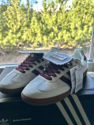Adidas Wales Bonner 40 - Helt nya Adidas x Wales Bonner sneakers i storlek 40 säljes. Exklusiv och eftertraktad modell med premiumdetaljer, vinröda detaljer och ponnyhårsinspirerad finish som ger skorna en unik look.  * Storlek: 40 🥾 * Innersula: ca 25 cm✅ * Skick: Helt nya / oanvända😁 * Originalbox och påse medföljer📦