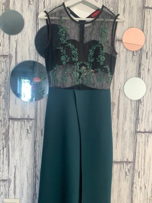 Grön jumpsuit med spets och brodyr - Stilren grön jumpsuit med vida ben och ärmlös topp i svart mesh med gröna broderade blommor. Toppen har transparent mesh och hjärtformad byst, vilket ger en trendig och elegant look. Perfekt för dig som vill sticka ut med en unik och modern outfit.