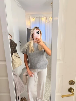 Grå kortärmad stickad tröja från Zara - Mysig och stilren grå loungewear-tröja med korta ärmar och rund hals. Tröjan har en avslappnad passform och är perfekt för chill dagar hemma. Materialet ser ut att vara mjukt och bekvämt, troligen bomull eller en bomullsblandning.