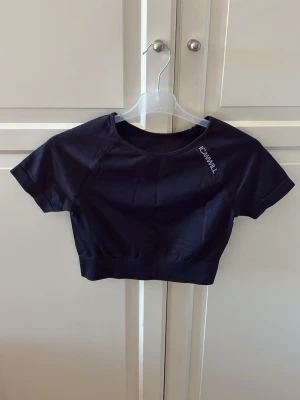 Svart crop top från ICANIWILL - Svart sportig crop top från ICANIWILL med korta ärmar och rund halsringning. Tillverkad i stretchigt funktionsmaterial som andas. Logga tryckt på bröstet. Snygg och bekväm passform. Storlek S. I fint skick. 