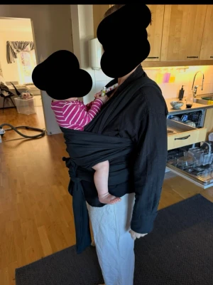 Svart bärsjal för bebis - En svart bärsjal i mjukt tyg, perfekt för att bära bebis nära kroppen. Sjalen knyts runt kroppen och ger bra stöd både fram och bak. Passar för dig som vill ha händerna fria och ändå ha barnet nära.