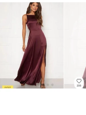 Vinröd långklänning med slits - Elegant vinröd långklänning i glansigt satinliknande material. Klänningen har smala axelband, öppen rygg med draperad detalj och hög slits framtill. Perfekt för dig som vill sticka ut med en stilren och lyxig look.