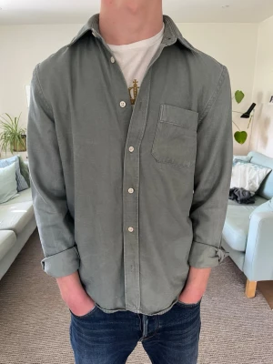 Grön Skjorta/Overshirt - Stilren grön skjorta med klassisk krage och bröstficka. Skjortan har långa ärmar och knäppning framtill med vita knappar. Perfekt för en avslappnad men snygg look.