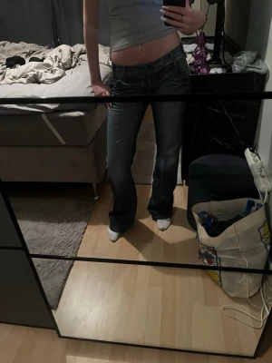 Mörkblå bootcut jeans med låg midja - Säljer ett par mörkblå bootcut jeans med låg midja och snygga detaljer på bakfickorna. Jeansen har knappar bak i midjan och klassisk femficksdesign. Perfekta för dig som gillar en avslappnad och trendig look. Finns dock skador i bak då som gått sönder. Nytt pris 1500