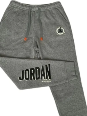 Grå Jordan mjukisbyxor - Snygga grå mjukisbyxor från Jordan med stor logga på benet och Jumpman-märke på höften. Byxorna har snörning i midjan med orange detaljer och är tillverkade i mjukt bomullsmaterial. Perfekta för en avslappnad och sportig look.