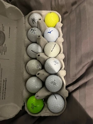 Golfbollar Vice/Mizuno. De flesta vice är Vice Pro Plus. Två färgade på köpet också. - Ett dussin golfbollar i äggkartong, mestadels vita men även några gula och en grön. 
