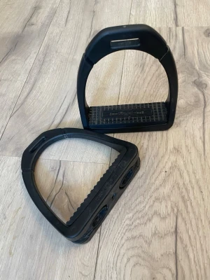 Svarta stigbyglar i plast - Ett par svarta stigbyglar från Hööks (compositi) i  tålig plast med räfflad fotplatta för extra grepp.. Snygg och enkel design som funkar till både träning och tävling.  Sparsamt använda - tvättas innan de skickas. (Kan även hämtas i Sjöbo) 