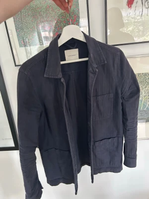 Mörkblå overshirt från A Days March - Stilren mörkblå overshirt från A Days March  i mjukt bomullstyg. Modellen har klassisk krage, tre utanpåliggande fickor framtill och raka ärmar. Perfekt lager-på-lager-plagg med avslappnad passform och minimalistisk design.