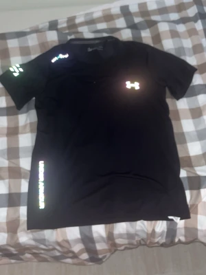 Svart tränings-tshirt Under Armour - Snygg svart tränings-tshirt från Under Armour med reflekterande logga på bröstet och ärmen. Tillverkad i funktionsmaterialet Threadborne HeatGear som andas och transporterar bort fukt. Perfekt för gymmet eller löprundan.