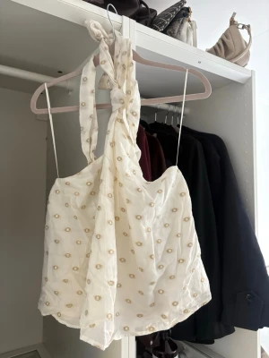 Vit linnetopp med knyt och broderi - Supersöt vit linnetopp med tunna axelband och knyt i nacken. Toppen har små broderade detaljer i beige och en luftig, flowy passform. 
