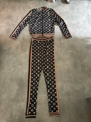 2-delad dress med text på. - 2-delad dress med ziptröja och byxor/leggings till. Svart med guldaktiga färger. Setet är helt nytt!