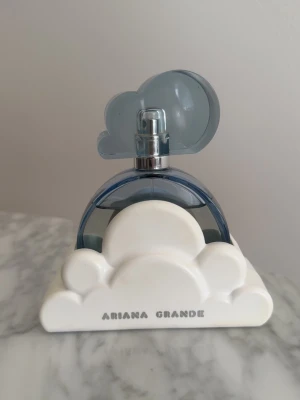 Ariana Grande Cloud parfym - Säljer en Ariana Grande Cloud parfym i 100ml med en unik flaska i blått och vitt. Flaskan har en halvmåneformad design med vita moln i plast och ett blått moln som lock. Perfekt för dig som gillar snygga och kreativa parfymflaskor.