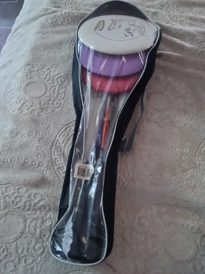 Badmintonset med 4 racketar och bollar, frisbees ingår också!  - Säljer ett komplett badmintonset med fyra racketar i färgerna lila och röd, samt tillhörande fjäderbollar och väska med transparent framsida. Perfekt för spel med vänner eller familj. Racketarna har svarta handtag och är lätta att bära med sig. Säljer även frisbees som syns i bilden, kan välja om man villa ha det eller inte. Bild tre visar en defekt på en av racketerna. 