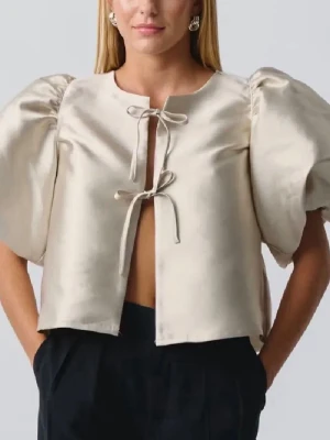 Champagne puffblus med knytning - Trendig blus från Gina i glansigt material med stora puffärmar och två knytband framtill. Blusen har rund halsringning och kort ärm med volym, perfekt för en statement-look.