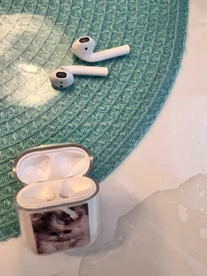Trådlösa vita hörlurar med kattmotiv - Säljer ett par trådlösa vita in-ear hörlurar med laddningsetui. Etuiet har en söt kattbild på framsidan. Hörlurarna har stilren design och passar perfekt till mobilen eller datorn. Smidiga att ta med överallt.