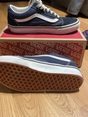 Vans Old Skool blåvita sneakers - Klassiska Vans Old Skool sneakers i marinblått och vitt med den ikoniska sidsvingen. Ovandelen är i canvas och mocka, med vita snören och gummisula med våffelmönster. 