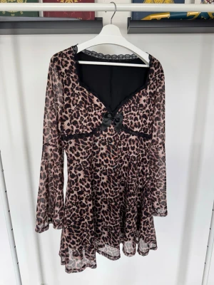 Leopardmönstrad kort klänning - Kort klänning med leopardmönster i beige och svart, transparenta långärmar och spetsdetaljer vid halsringningen. 