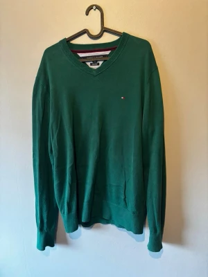 Grön Tommy Hilfiger v-ringad tröja  - En Tommy Hilfiger v-ringad tröja. Använd vid ett fåtal tillfällen så i bra skick. Tröjan är storlek L. Perfekt till sena sommar kvällar. Bara att skriva om det skulle dyka upp nån fråga:)