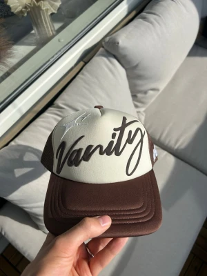 vanitywrld trucker keps - Brun och kräm vit trucker keps, puffprint logga på framsidan med broderad text på sidan